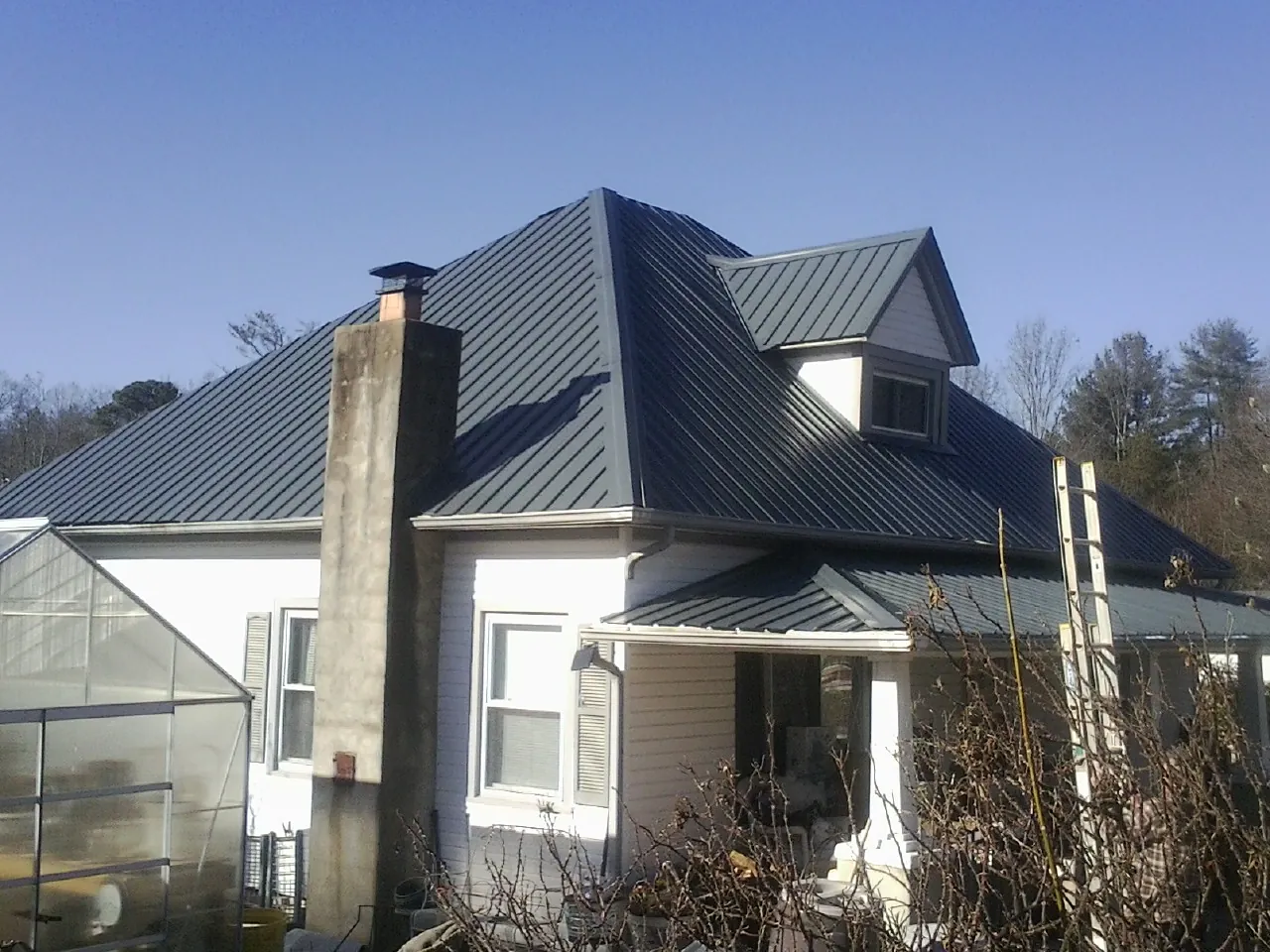 Dark blue standing seam metal roof on a white farmhouse with dormer — Slate & Tile Roof Repair by Roofing Brothers in Bay Shore