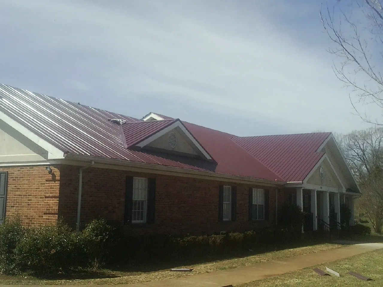 Red metal roof with gabled entries on a long brick building, from a Hail Damage Roof Repair job in Bay Shore