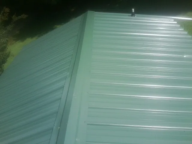 New green metal panels meeting at the ridge of a roof — Flat Roof Repair work by our crew in Bay Shore