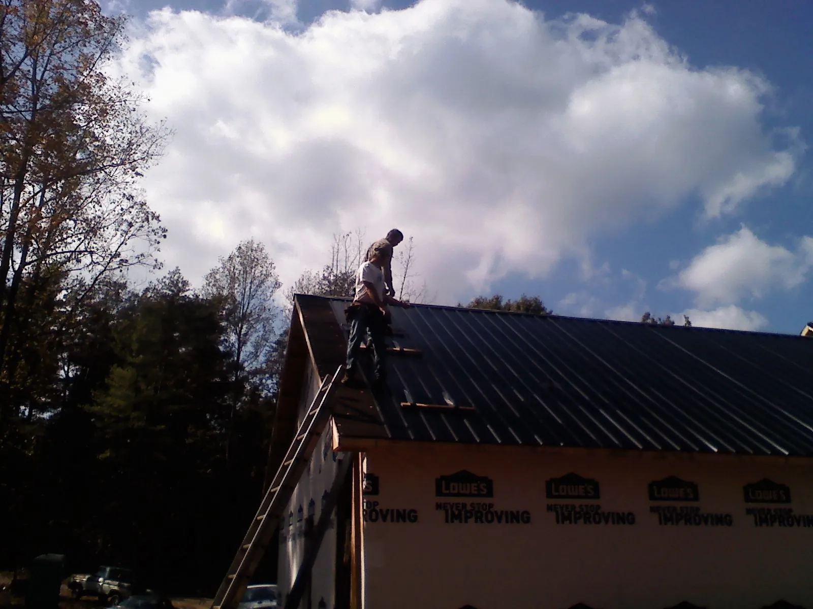Roofer fastening dark metal panels high against a cloudy sky, from a Roof Inspection job in Bay Shore