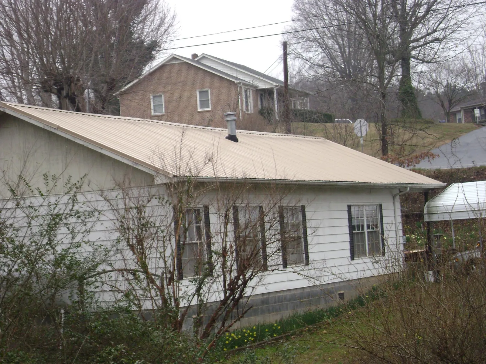 Tan metal roof on a white sided house set into a hillside — Commercial Roofing by Roofing Brothers in Bay Shore