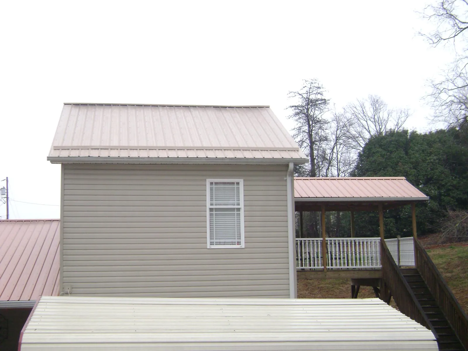 Tan metal roofs on a two story addition and attached porch, from a Roof Replacement job in Bay Shore
